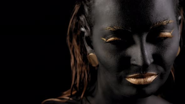 Closeup of a Young Beautiful Woman's Face with Black and Gold Paint on Her Skin