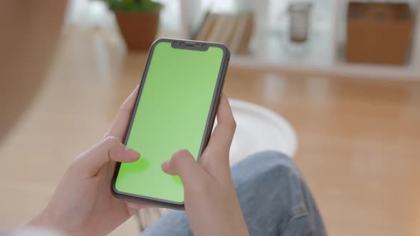 Woman holding mockup smartphone green screen with type message on the sofa at home.