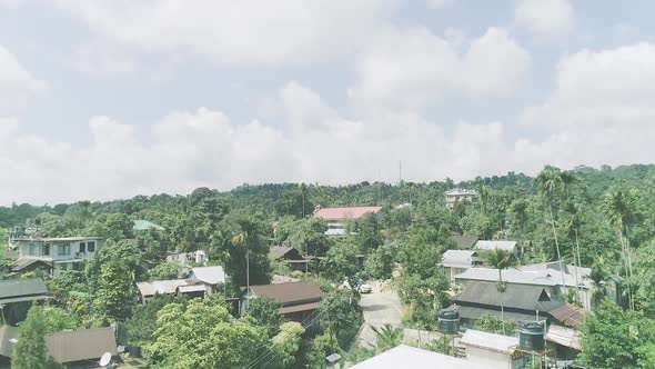 Cloudy sky over village with houses surrounded by tall trees of tropical forest