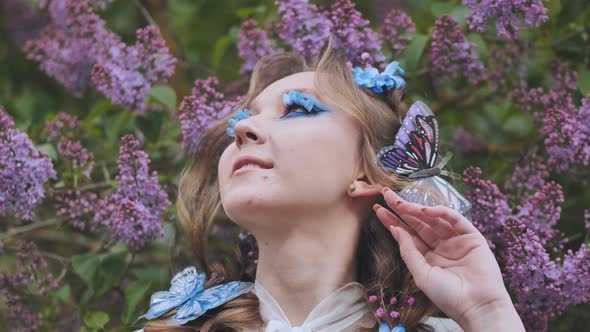 A Young Girl Poses in Lilac with a Beautiful Hairstyle of Flowers and Butterflies