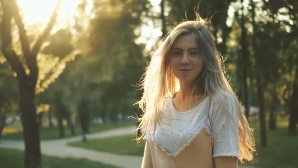 Attractive Young Woman Goes Down the Street in a City Park, Turns to Camera and Smiles.