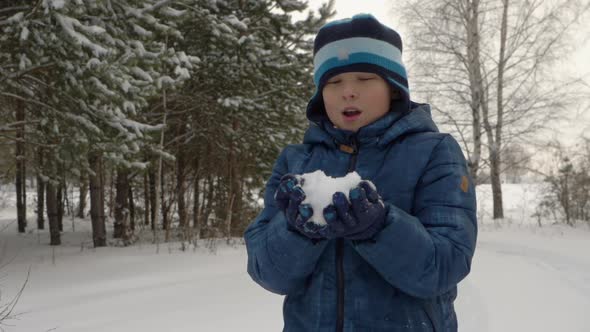 Boy Teenager Blowing and Throwing Up Snow While Winter Walk in Snowy Forest