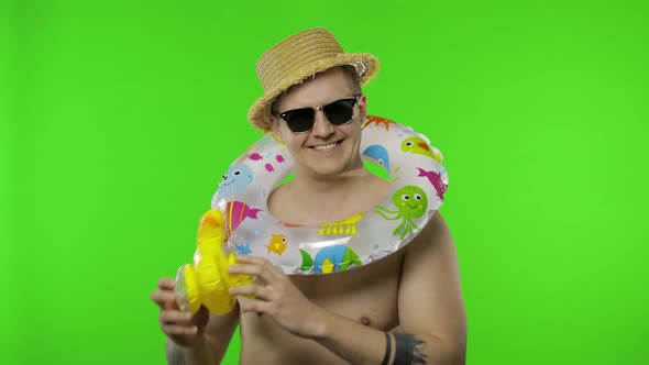 Shirtless Young Man Tourist with Swimming Ring on Shoulders Plays with Duck Toy