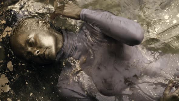 Art Performance with Golden Dye Woman with Face Hands and Hair Covered Gold Is Lying in Water