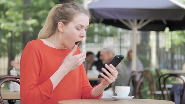 Young Woman Upset By Loss on Smartphone Sitting in Cafe Terrace