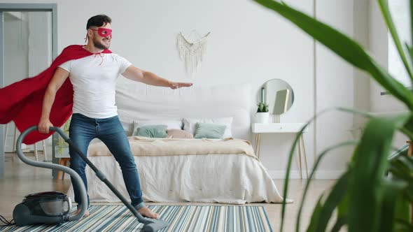 Joyful Guy in Superman Costume Cape and Mask Cleaning Carpet with Vacuum Cleaner