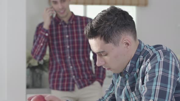 Close-up Side View of Handsome Caucasian Man Sitting at the Table Reading and Eating Red Apple. His