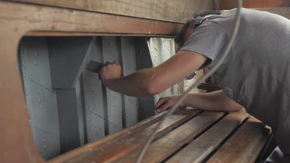 Young man painting interior of wooden boat with aluminium wood primer