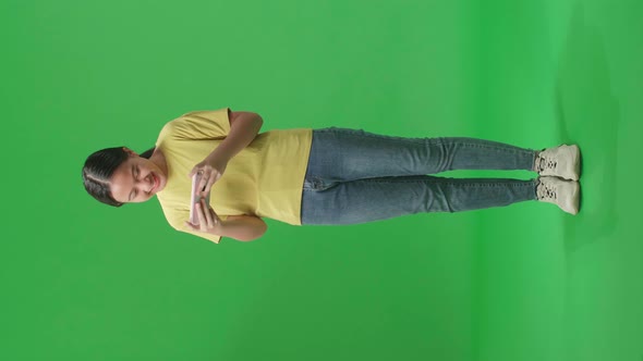 Full Body Of Laughing Young Asian Kid Girl Looking At The Phone On Green Screen In The Studio alt