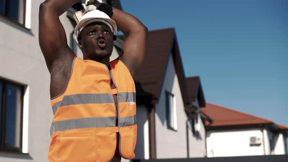 Muscular African American in uniform waving a sledgehammer at a construction site.
