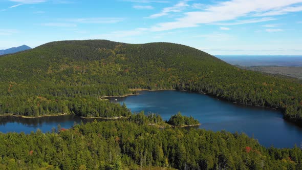Aerial drone shot orbiting over a calm blue forest lake with a small island and thick green forest i
