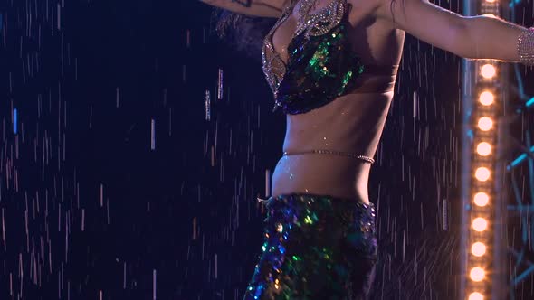 Sexy Oriental Dancer Enjoys Belly Dancing Under the Raindrops in a Dark Studio with Blue Lights