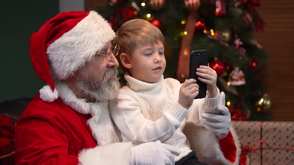 Santa Claus with a Little Boy Clicking on a Smartphone Choosing a Christmas Present on the Internet