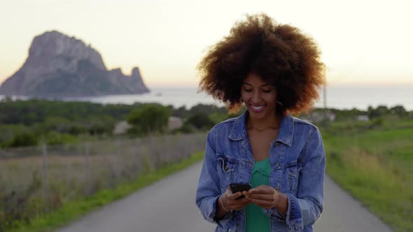 Smiling woman using smartphone on road at sunset
