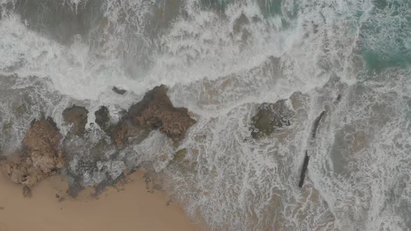 Cinematic aerial top down lowering of waves breaking on submerged rocks at Calheta Porto Santo