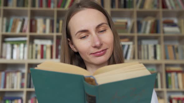 Young Woman Student Reading a Book in a Library