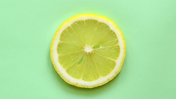 Slice of lemon rotating top view on green background