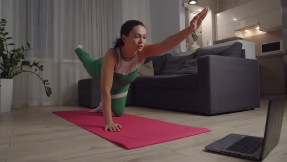 Woman in Sportswear Doing Bird Dog Exercise Looking at Laptop Indoors