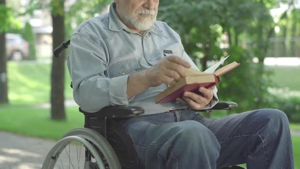 Unrecognizable Paralyzed Senior Man Turning Book Page and Reading Out Loud. Old Grey-haired Male