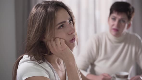 Annoyed Young Caucasian Woman Listening To Her Mother Scolding Her From the Background. Daughter and