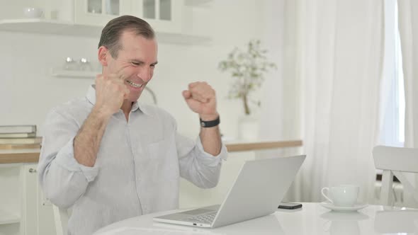 Middle Aged Man Celebrating Success on Laptop at Home 