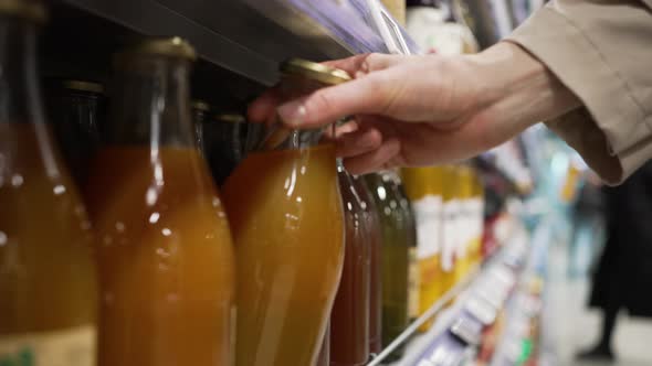 Woman Looks for Fresh Juice Taking Glass Bottle From Shelf