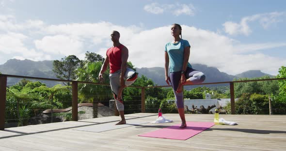 Relaxed biracial couple on terrace, practicing yoga together on mats