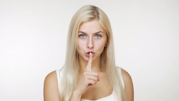 Serious Young Blond Woman with Long Hair in Casual Clothes Holding Index Finger on Lips Asking to