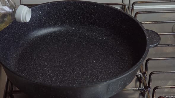 Cook pours sunflower oil into a frying pan. Kitchen pan stands on Stove