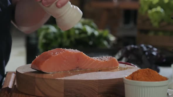 Cooking seafood in kitchen. cook pours pepper on juicy fresh salmon steaks