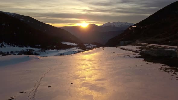 Drone traveling above the snow through the Cortals valley in Andorra, the light of the sunset is ref