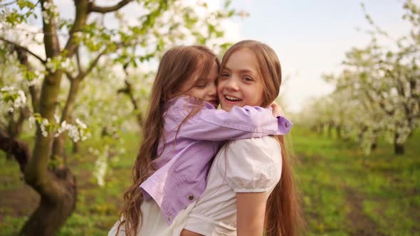 Two Girls Sisters Have Fun and Cuddle in the Garden with Flowering Trees