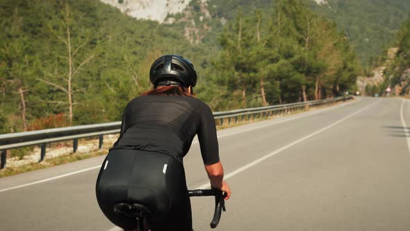 Athletic cyclist stepping on pedals of road bicycle during intense mountain cycling training
