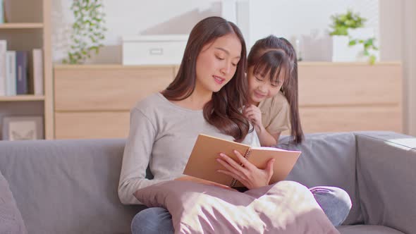 An Asian mom and her kid are reading together. Mom is teaching her child