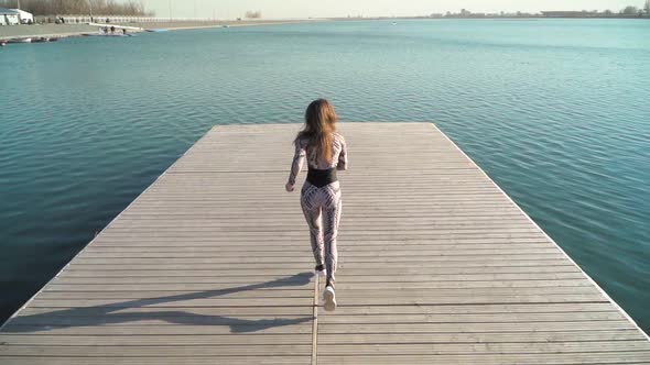 Woman Athlete with a Beautiful Figure Runs on the Pier of the Lake. Slow Motion.