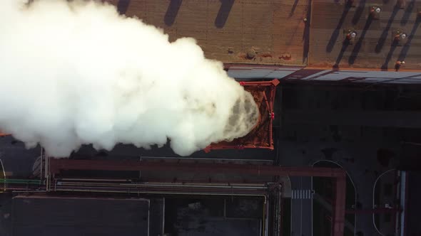 Top-down aerial view of a chimney of an industrial plant with white smoke polluting the air.