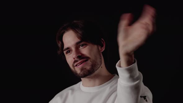 Trendy Young Man waving towards camera, welcoming gesture, close, black background