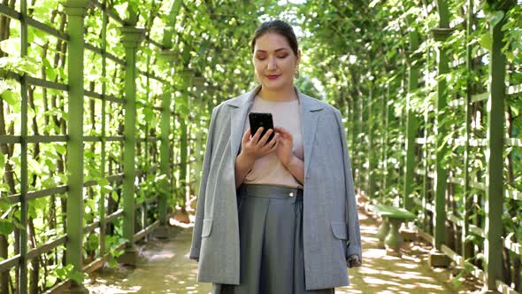 Young Woman with Phone Under a Living Arch in the Garden