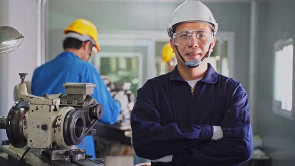 Portrait of mechanical workers man wear hardhat, crossed arm looks at camera while work in factory.