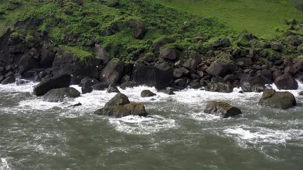 Coastline in Vik, Iceland with waves hitting big, black rock with drone video moving sideways.