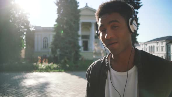 Portrait of Young Stylish Hipster Black Man in White Headphones and Sun Glasses Dancing Outdoor in