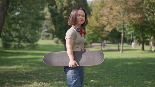 Confident Caucasian Little Woman Standing with Skateboard in Park Looking at Camera Smiling