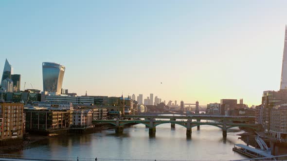 Aerial rising drone shot over Thames river bridges towards canary wharf at sunrise