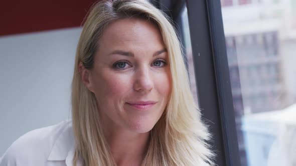 Portrait of caucasian businesswoman looking at camera and smiling by window in office