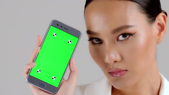 Beautiful Asian businesswoman showing smartphone with green screen