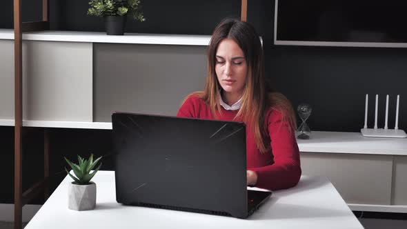 Young Woman in a Burgundy Sweater Using a Laptop at Modern Interior Office