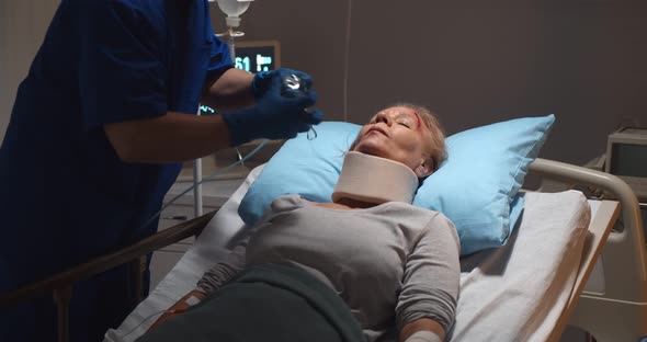 Nurse Putting Oxygen Mask on Elderly Injured Woman Patient Lying in Hospital Bed