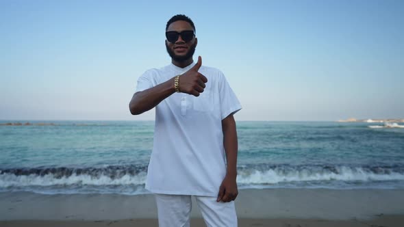 Portrait of Confident African American Man in Sunglasses Showing Thumb Up Standing on Sandy Beach