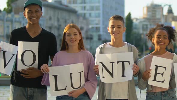 Group of Multiracial Teenagers Hold Volunteers Sign in Hands, Smiling on Camera