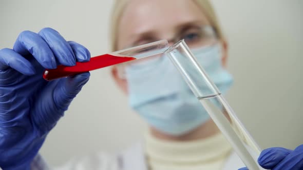 A Scientist Wearing a Medical Mask Pours Blood Into a Glass Flask with a Special Drug to Conduct